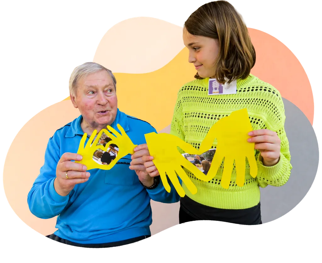 Ein Bewohnerpartner und sein Partnerkind begegnen sich lächelnd und zeigen gemeinsam gestaltete Erinnerungsbilder.